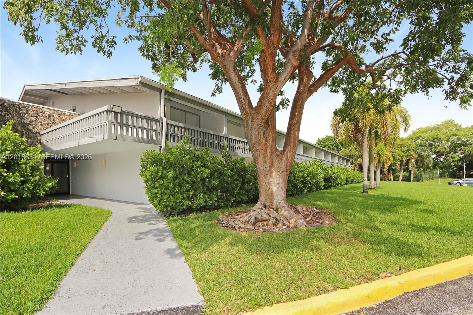 A two-story apartment building features a balcony, a large tree, and a concrete walkway — 750 NE 195th St, Miami FL 33179, MIAMI, FL