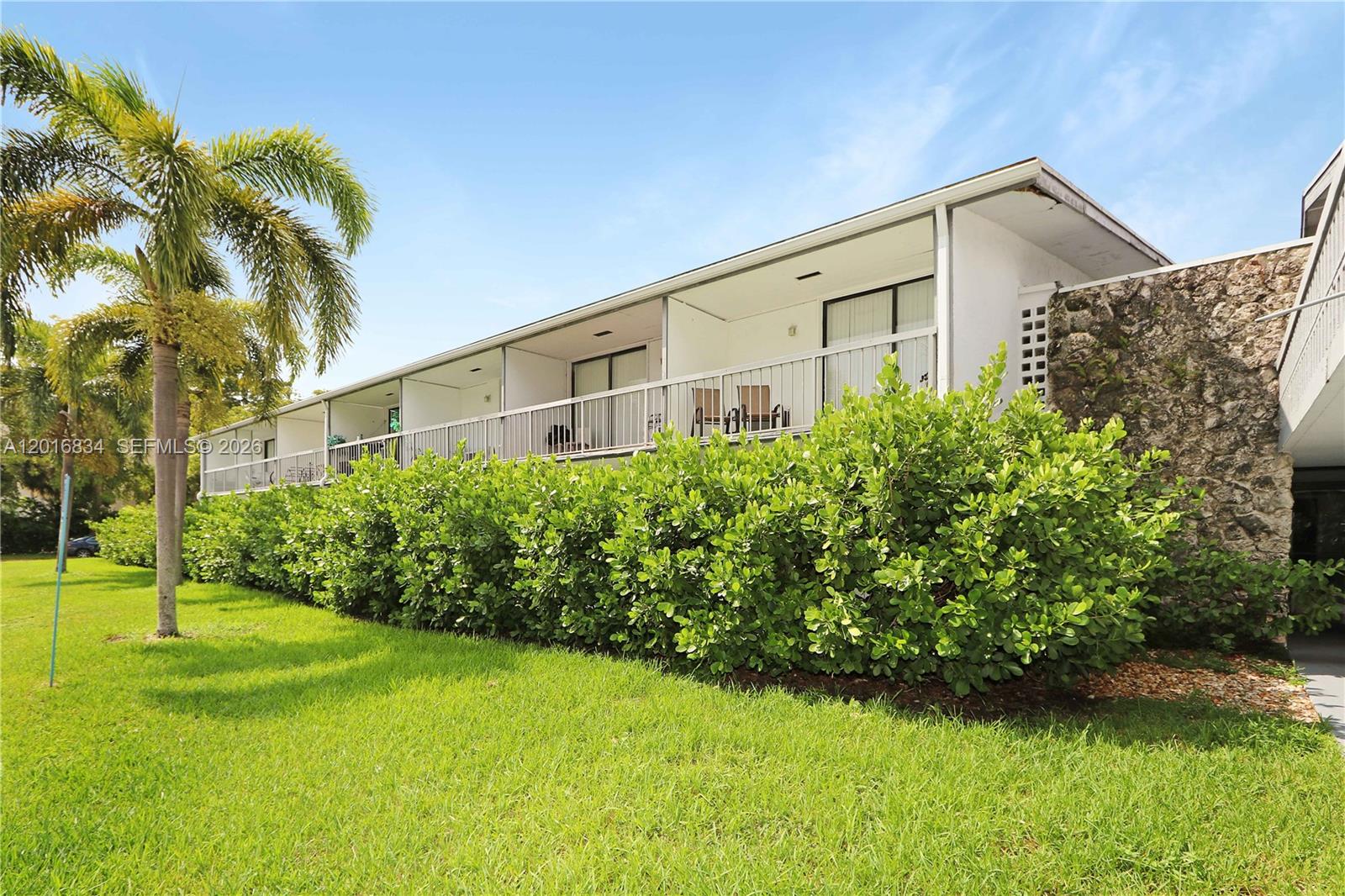 A two-story apartment building features a balcony with metal railings above a dense hedge — 750 NE 195th St, Miami FL 33179, MIAMI, FL