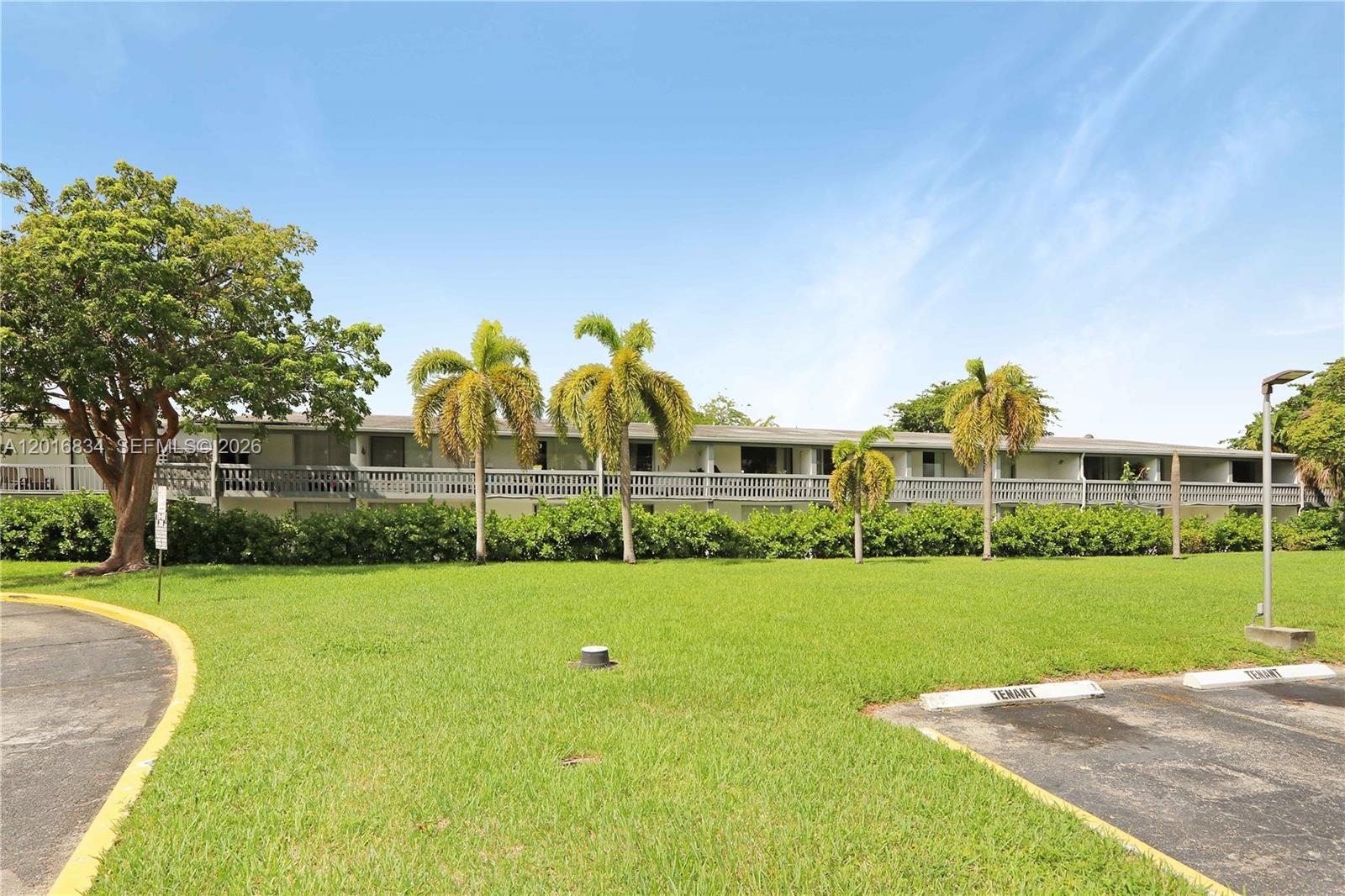 A multi-story apartment building features a long balcony, palm trees, and a grassy lawn — 750 NE 195th St, Miami FL 33179, MIAMI, FL