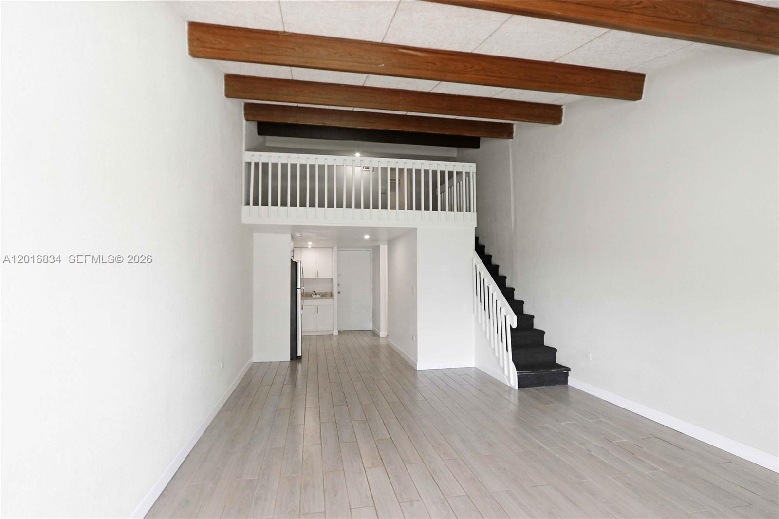 A living area features wood-look flooring, exposed ceiling beams, a staircase, and a loft space — 750 NE 195th St, Miami FL 33179, MIAMI, FL