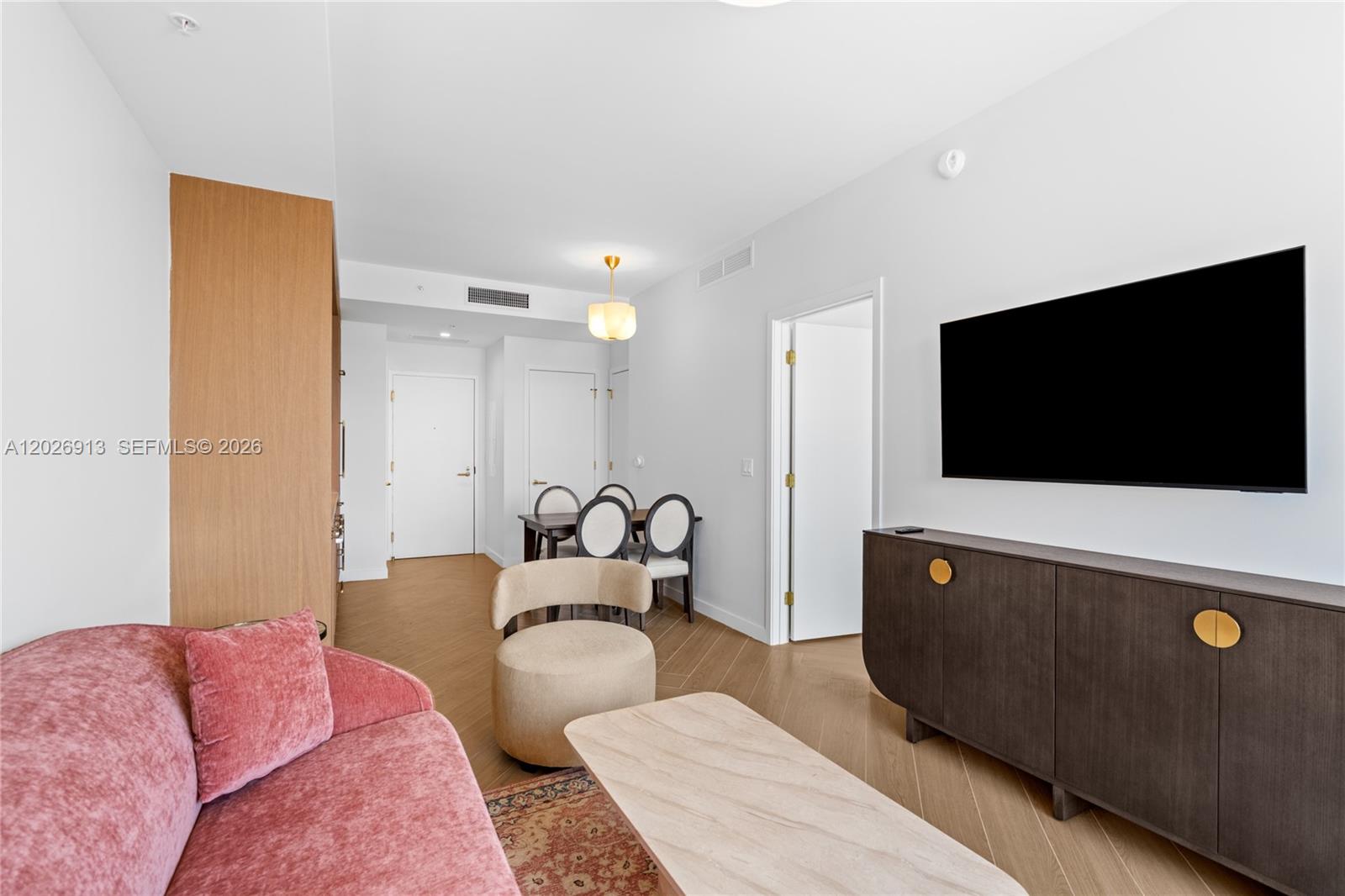 A living room features a pink sofa, a beige armchair, and a dark wood media console — 2700 NW 2nd Ave # 717, Miami FL 33127, MIAMI, FL
