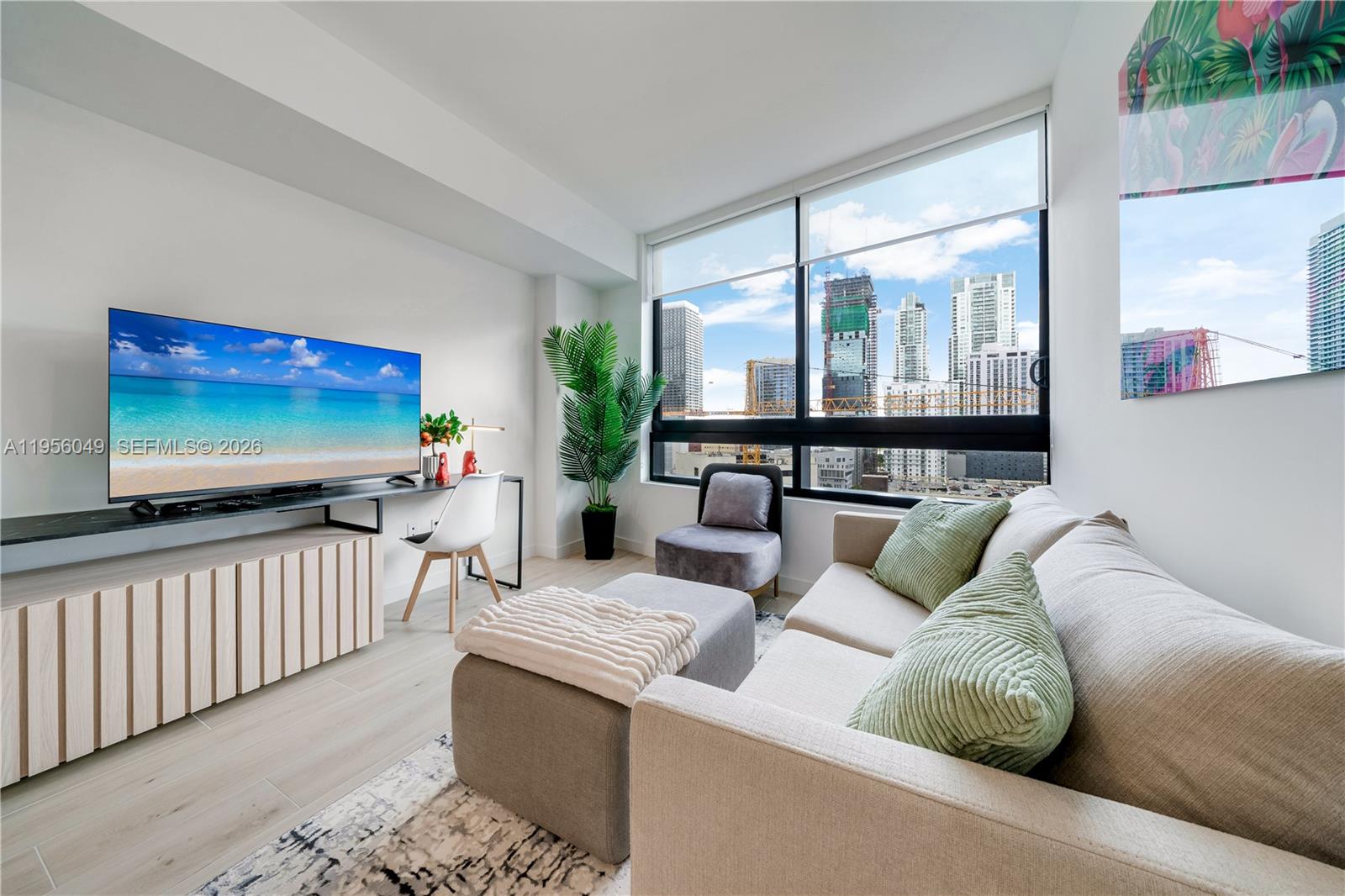 A modern living room features a sofa, television, desk, and floor-to-ceiling windows with city views — 225 N Miami Ave # 1707, Miami FL 33128, MIAMI, FL