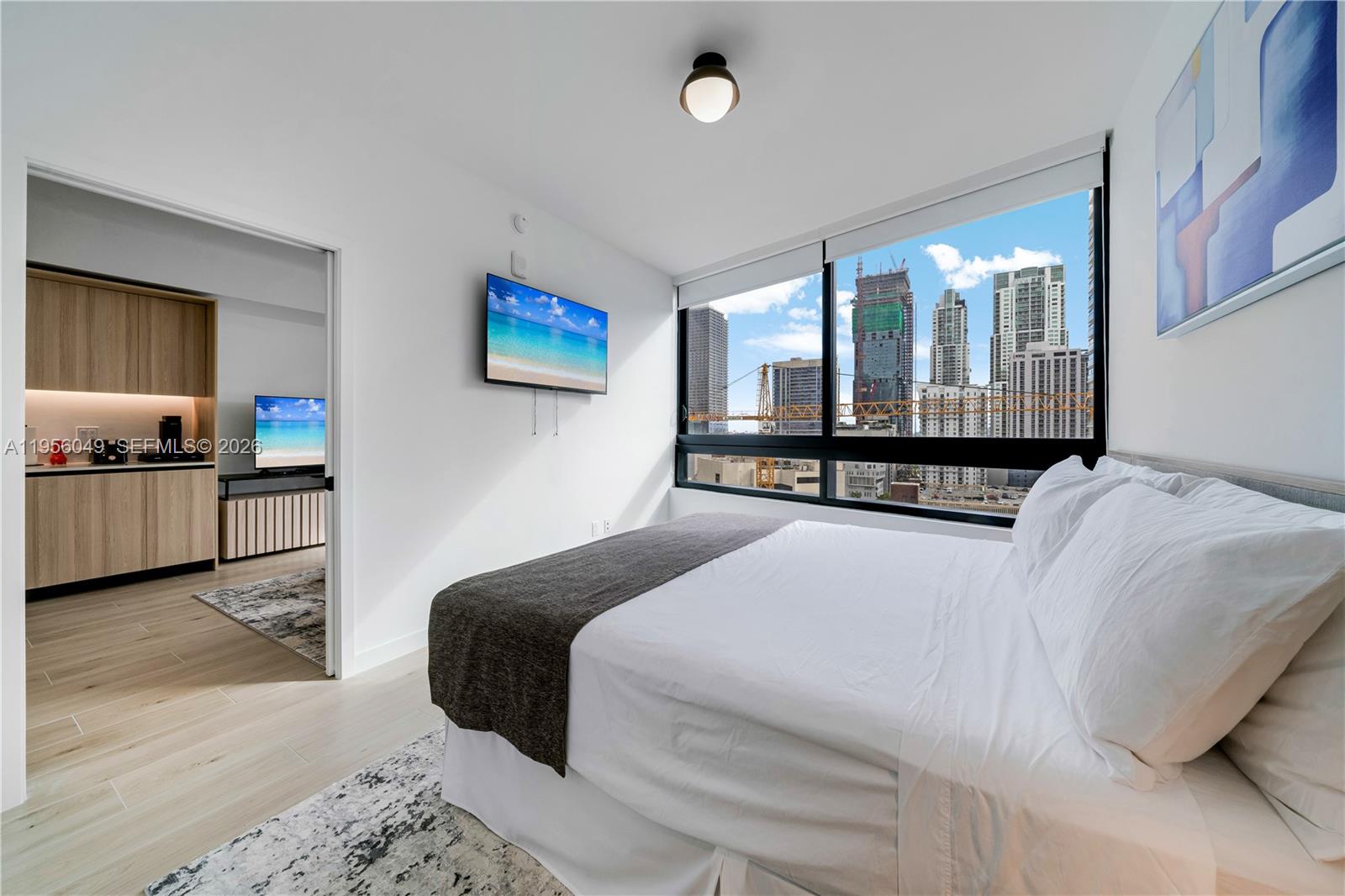 A bedroom with a bed, wall-mounted television, and a window view of city construction — 225 N Miami Ave # 1707, Miami FL 33128, MIAMI, FL