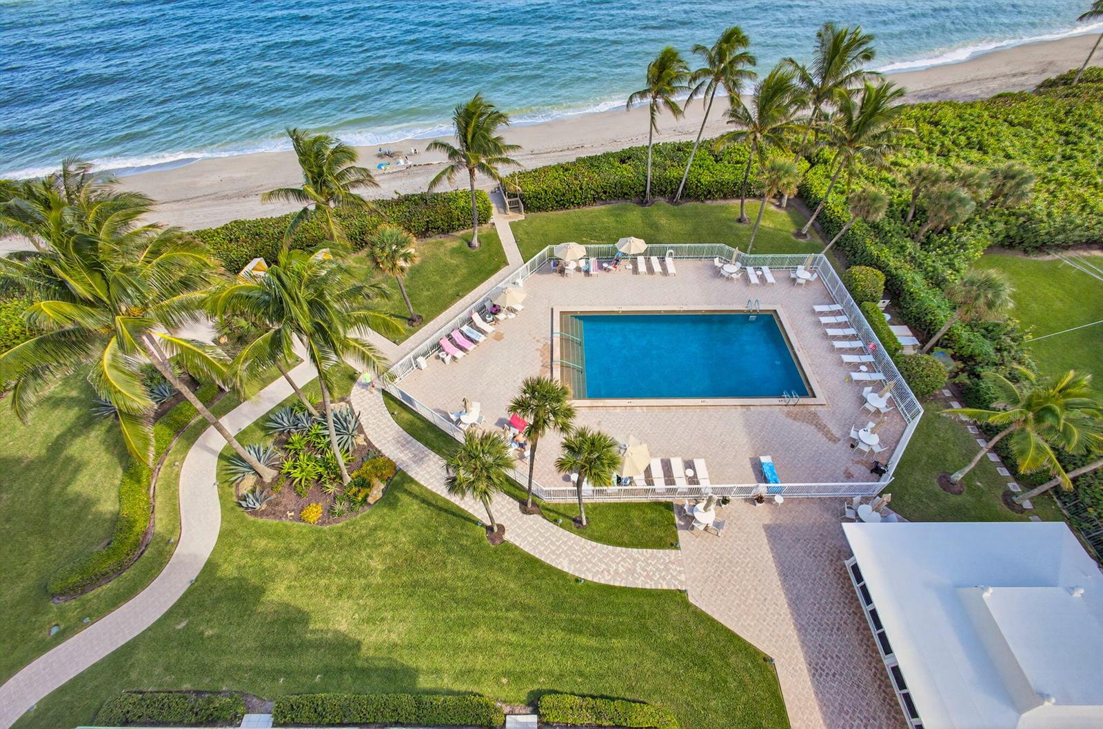 An aerial view of a rectangular swimming pool surrounded by lounge chairs, palm trees, and landscaping — 500 Ocean Drive # 11b, Juno Beach FL 33408, JUNO BEACH, FL