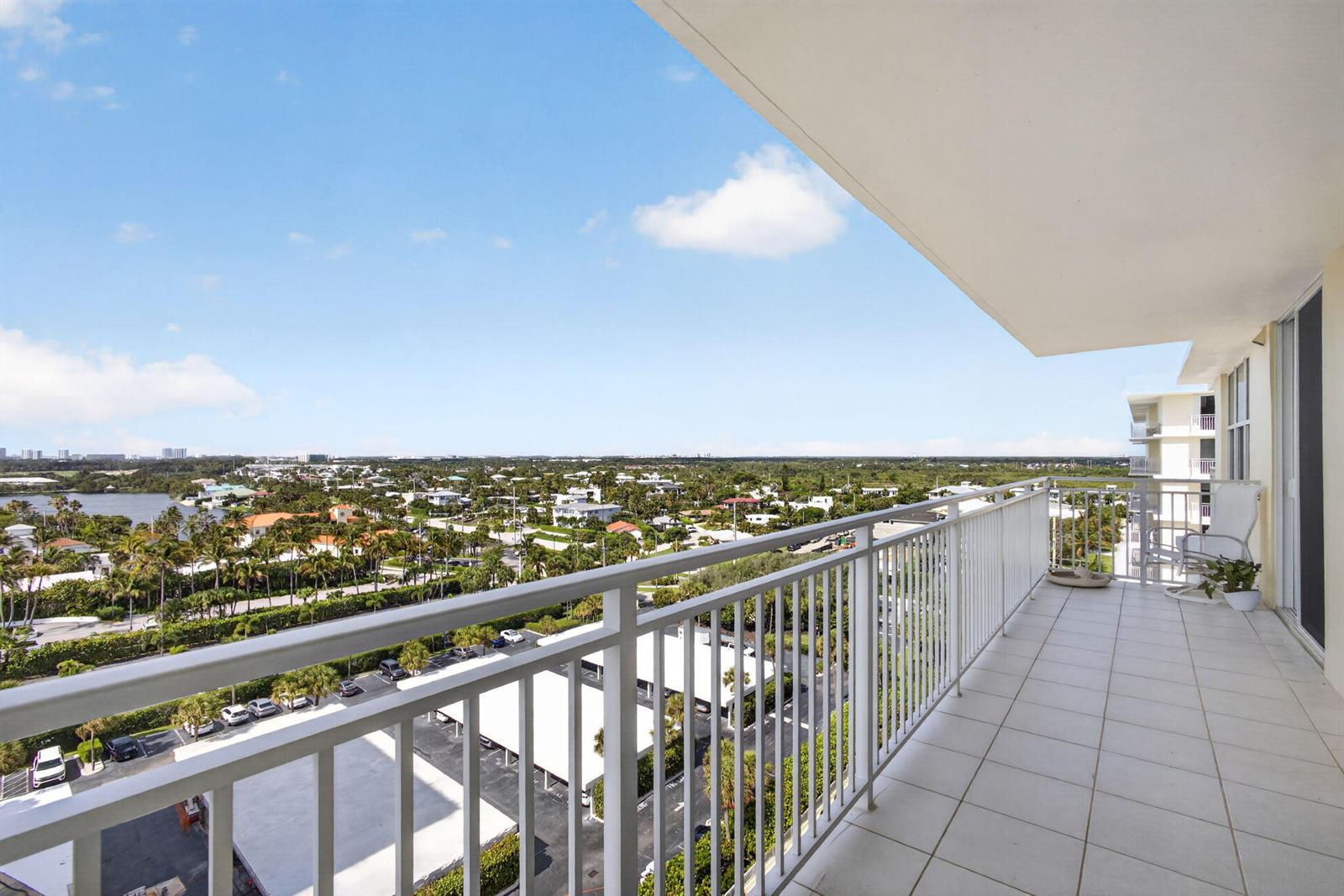 A high-rise balcony with white railings overlooks a suburban landscape and a parking lot — 500 Ocean Drive # 11b, Juno Beach FL 33408, JUNO BEACH, FL