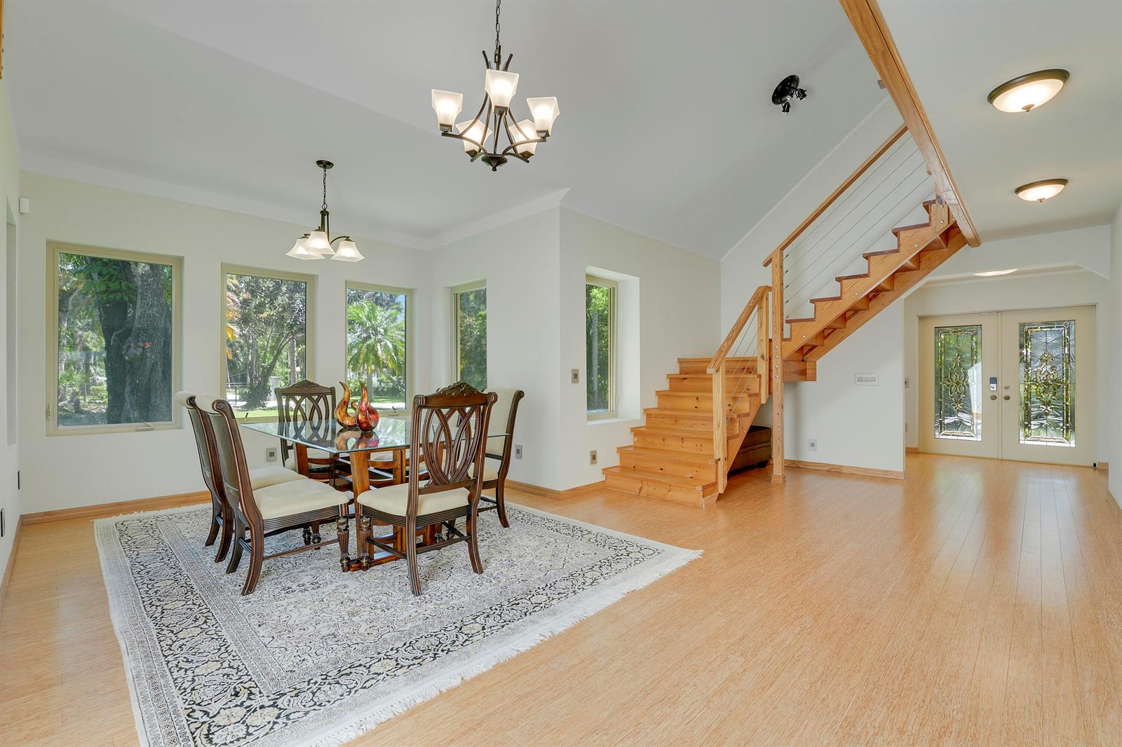 A dining area with a glass table, wooden staircase, and light-colored wood flooring — 12263 Sandy Run, Jupiter FL 33478, JUPITER, FL