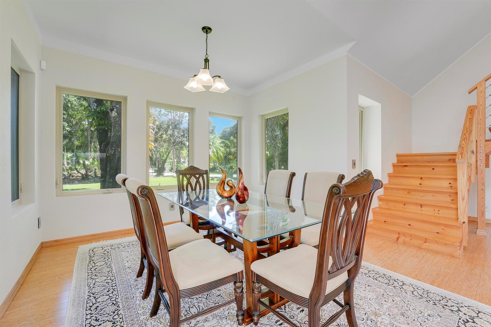 A dining room with a glass-topped table, wooden chairs, a patterned rug, and wooden stairs — 12263 Sandy Run, Jupiter FL 33478, JUPITER, FL