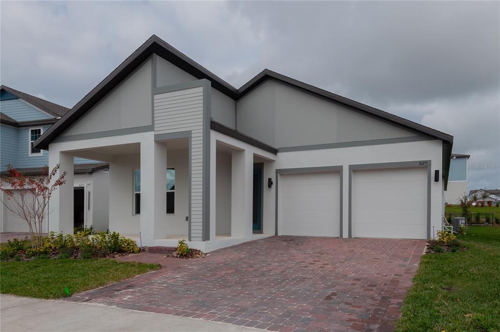 A modern single-story house features a two-car garage, a covered entryway, and a brick driveway — 16271 SILVER GROVE BLVD, WINTER GARDEN, FL