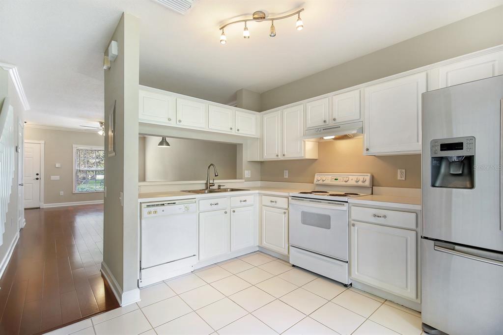 A kitchen with white cabinets, white appliances, and tile flooring, opening to a living area — 2403 LAKE WOODBERRY CIRCLE, BRANDON, FL