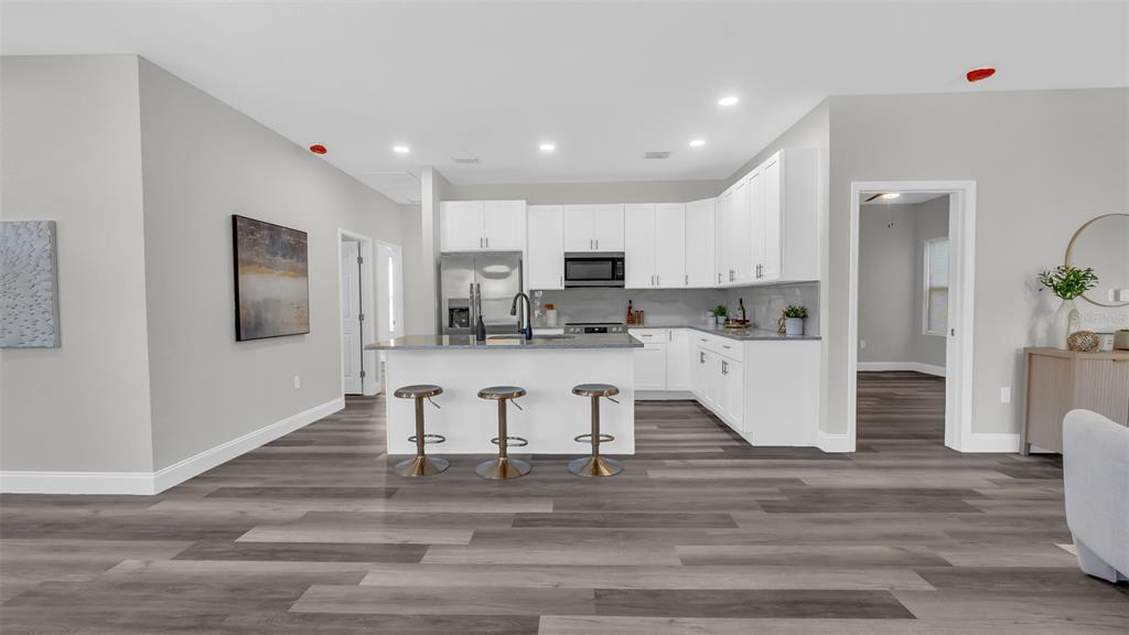 A modern kitchen features white cabinetry, a central island with three stools, and wood-look flooring — 1901 31ST STREET S, ST PETERSBURG, FL