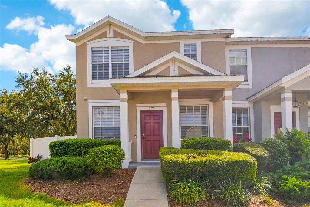 A two-story townhouse with a tan stucco exterior, a maroon front door, and manicured landscaping — 3314 BROKEN BOW DRIVE, LAND O LAKES, FL