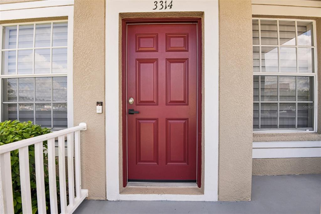 A red front door with six panels is centered between two windows on a porch — 3314 BROKEN BOW DRIVE, LAND O LAKES, FL