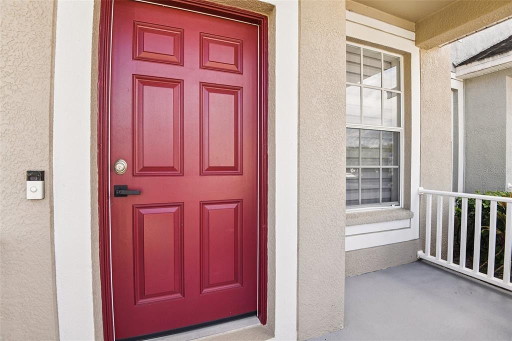 A red front door with a smart doorbell sits on a porch with white railings — 3314 BROKEN BOW DRIVE, LAND O LAKES, FL