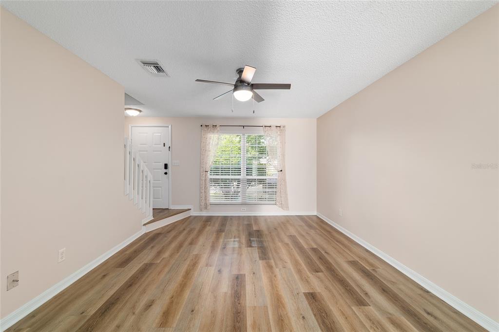 An empty living room features light-colored walls, wood-look flooring, a ceiling fan, and a window — 1701 SE 24TH ROAD UNIT 102, OCALA, FL