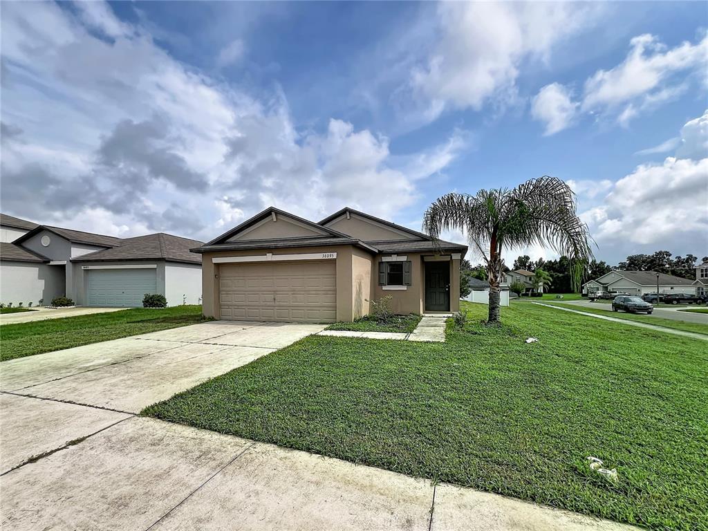 A tan single-story house with a two-car garage and a palm tree in the front yard — 36095 CARRIAGE PINE COURT, ZEPHYRHILLS, FL