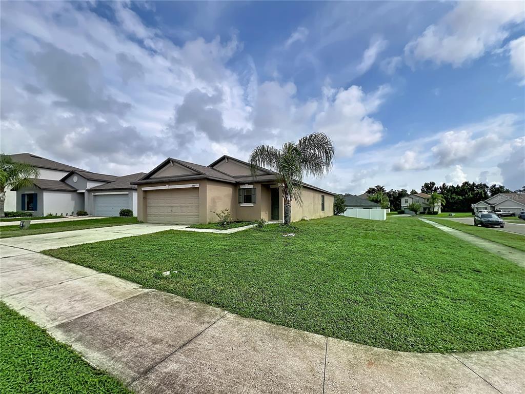 A single-story suburban house with a tan exterior, two-car garage, and a front lawn — 36095 CARRIAGE PINE COURT, ZEPHYRHILLS, FL