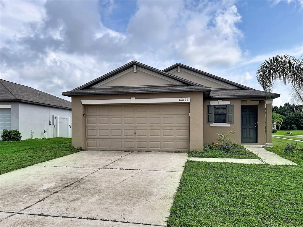 A tan, single-story suburban house features a two-car garage and a front entrance — 36095 CARRIAGE PINE COURT, ZEPHYRHILLS, FL