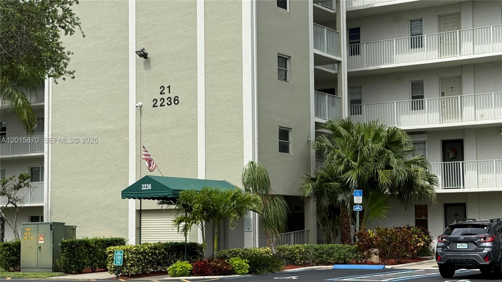 A multi-story apartment building exterior features a green awning, balconies, and a parking area — 2236 N Cypress Bend Dr # 207, Pompano Beach FL 33069, POMPANO BEACH, FL
