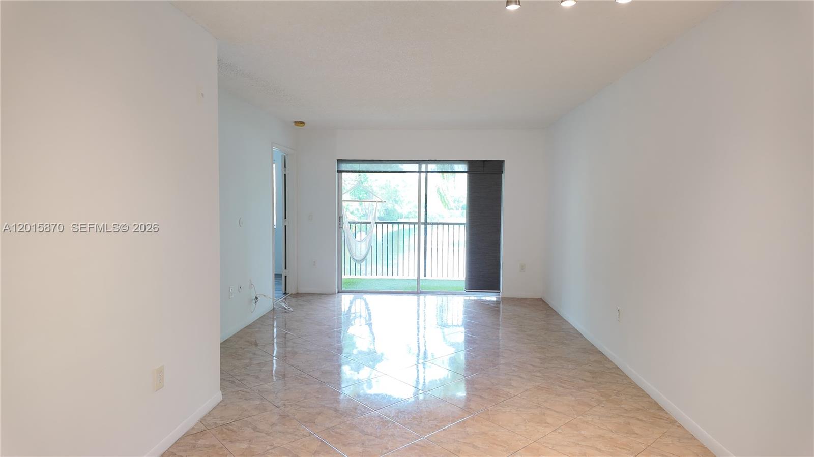 An empty living room features light-colored tile flooring, white walls, and a sliding glass door — 2236 N Cypress Bend Dr # 207, Pompano Beach FL 33069, POMPANO BEACH, FL