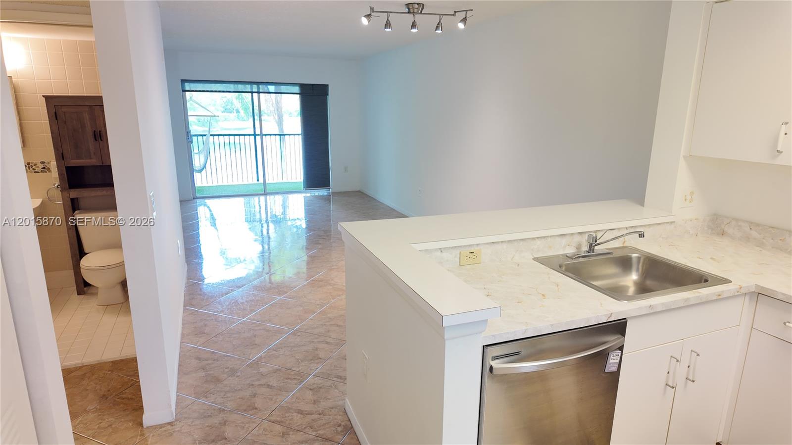 A kitchen with a stainless steel dishwasher overlooks a living area with tile floors — 2236 N Cypress Bend Dr # 207, Pompano Beach FL 33069, POMPANO BEACH, FL