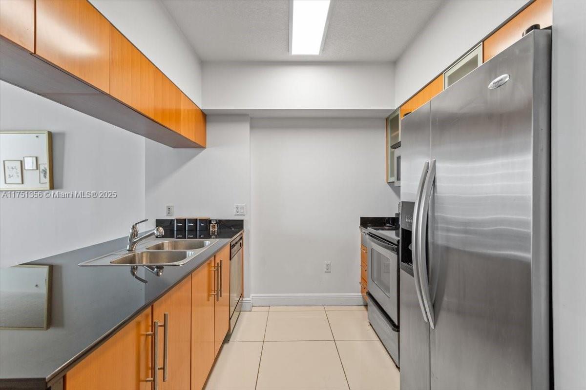 A galley kitchen features light wood cabinets, black countertops, and stainless steel appliances — 1750 N Bayshore Dr # 4809, Miami FL 33132, MIAMI, FL