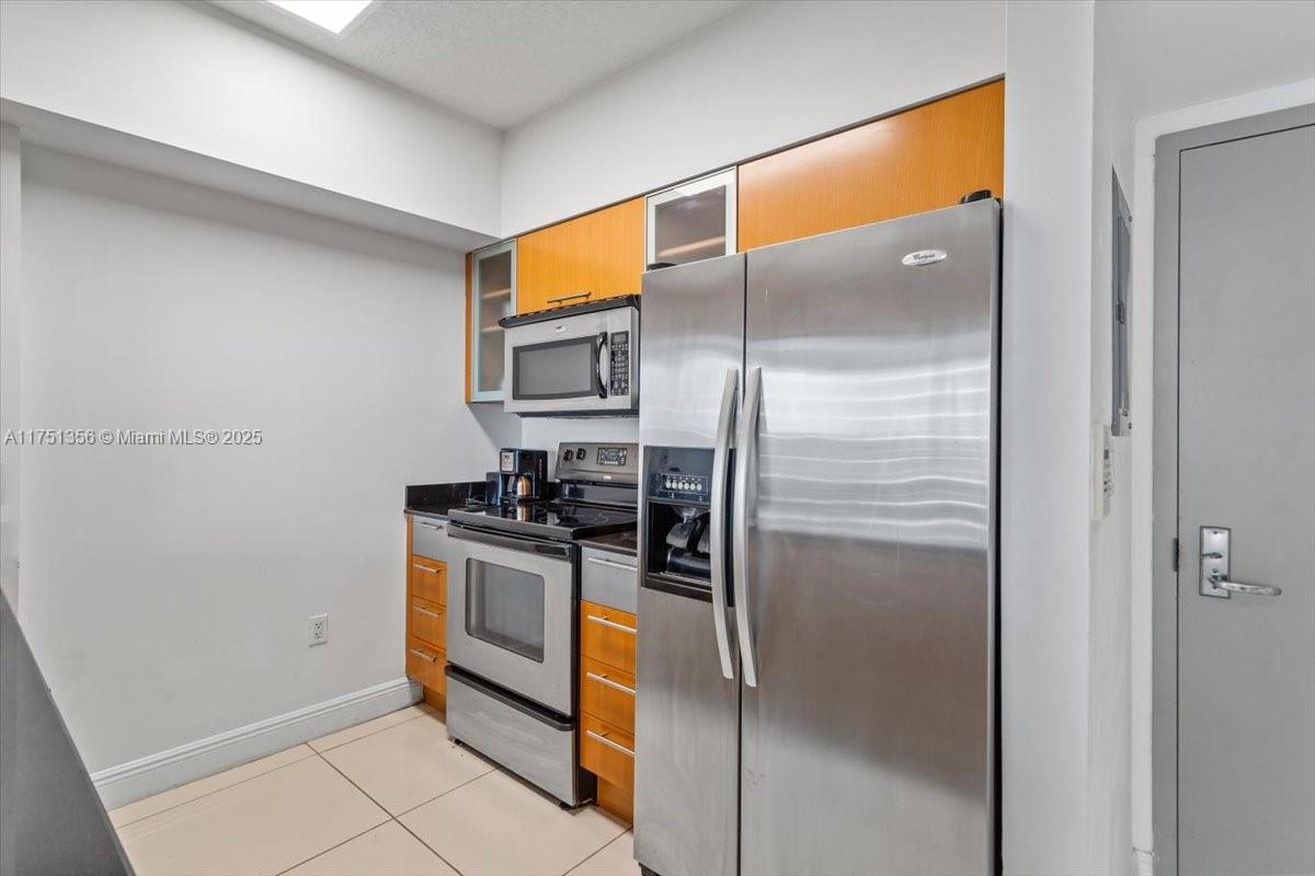 A kitchen features stainless steel appliances, wood-toned upper cabinets, and light-colored floor tiles — 1750 N Bayshore Dr # 4809, Miami FL 33132, MIAMI, FL