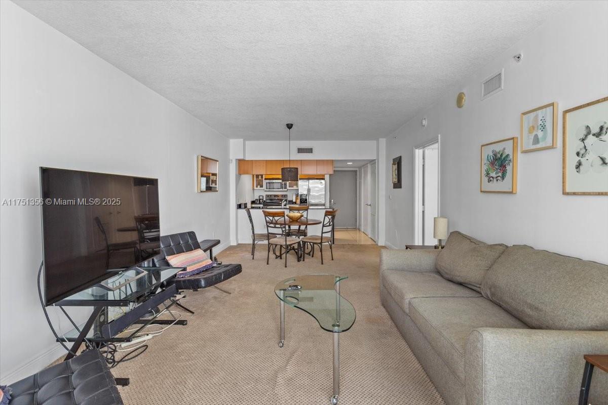A living room with beige carpet, a sofa, a television, and an adjacent dining area — 1750 N Bayshore Dr # 4809, Miami FL 33132, MIAMI, FL