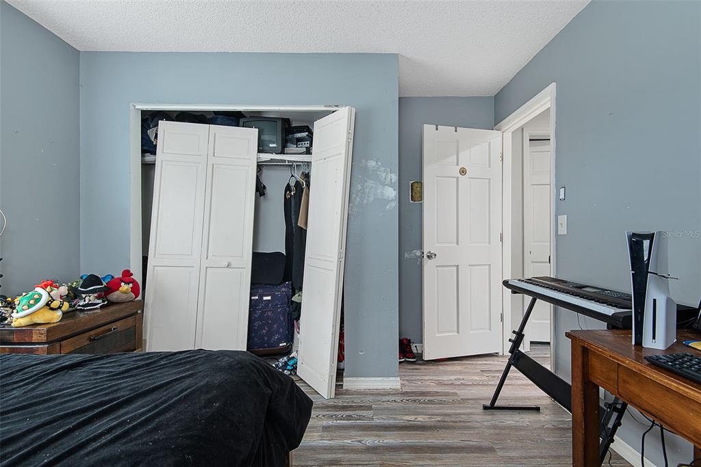 A bedroom features gray walls, wood-look flooring, a closet with folding doors, and a keyboard stand — 326 WELLINGTON DRIVE, PALM COAST, FL