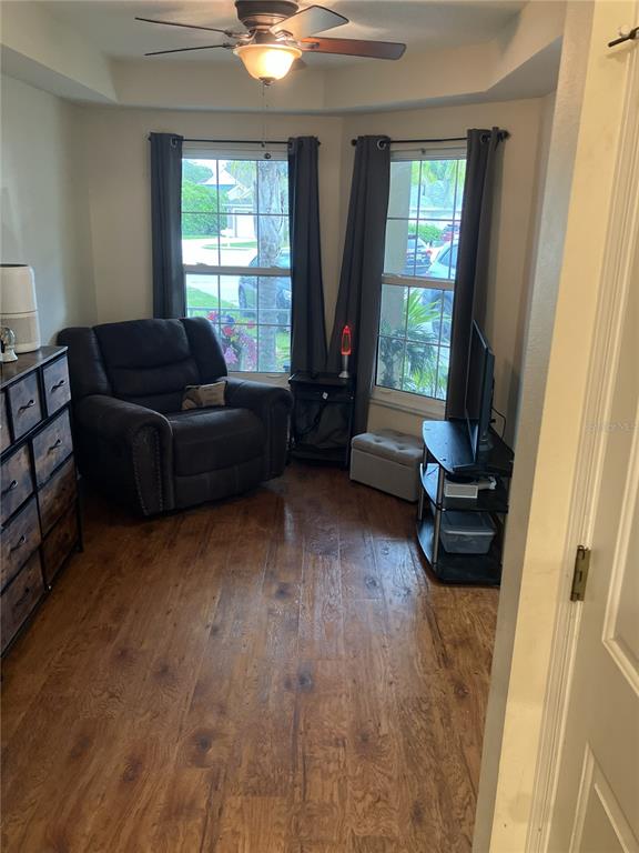 A room with wood-look flooring, a dark recliner, a television stand, and two windows — 28511 SEASHELL COURT, WESLEY CHAPEL, FL
