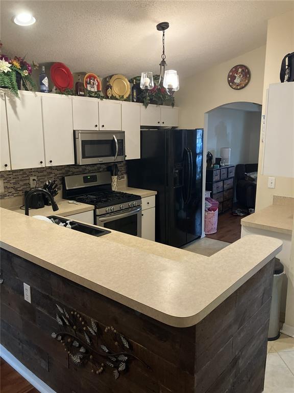A kitchen features white cabinets, black appliances, a wood-paneled breakfast bar, and a tiled backsplash — 28511 SEASHELL COURT, WESLEY CHAPEL, FL