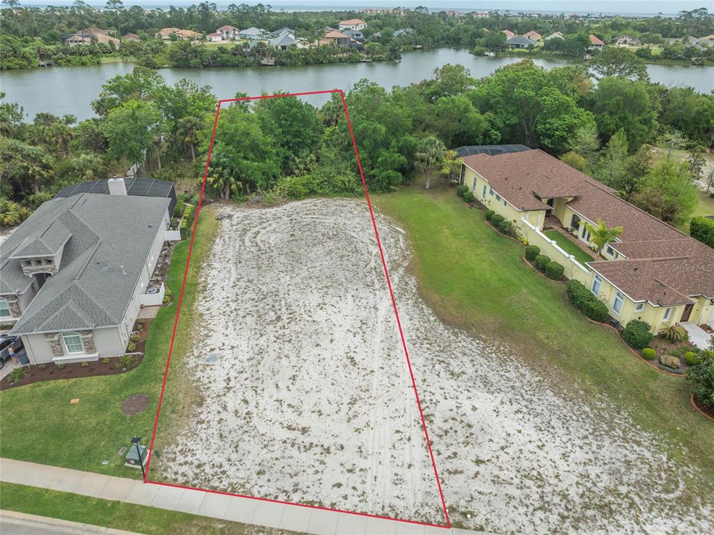 An aerial view shows a vacant, sandy residential lot outlined in red between two houses — 48 N LAKEWALK DRIVE, PALM COAST, FL