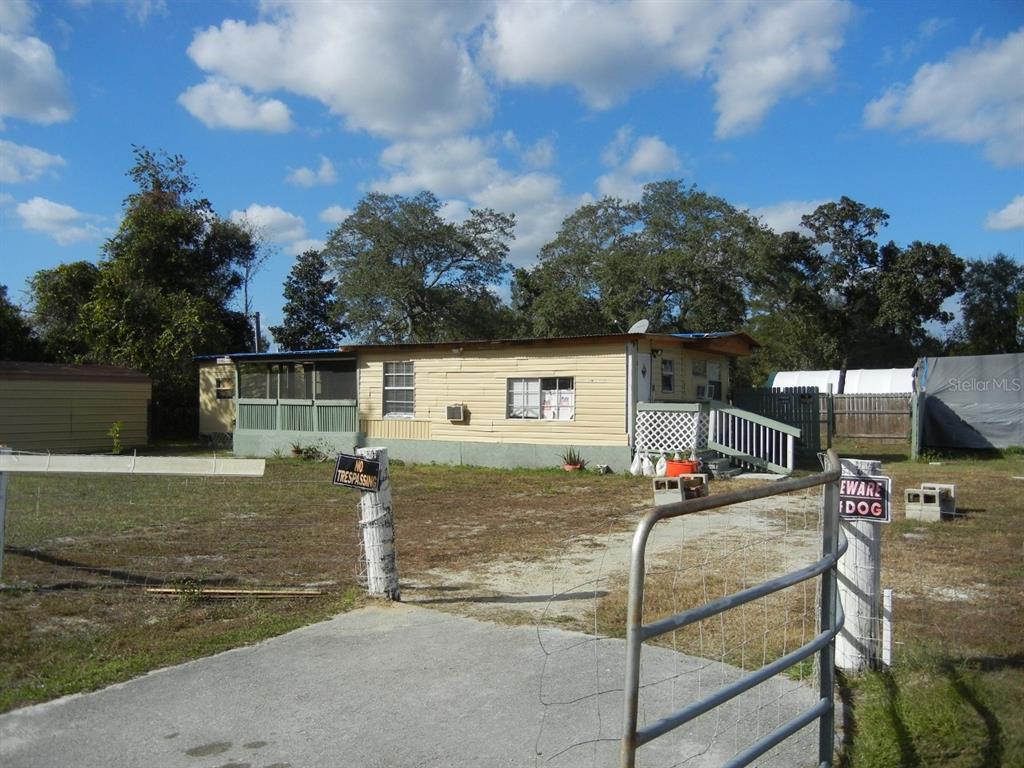 A single-story mobile home with a screened porch and a gated gravel driveway — 27945 VEVA AVENUE, PAISLEY, FL