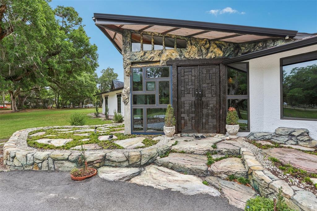 The exterior of a modern house features a stone facade, unique geometric windows, and landscaping — 27616 MILLER ROAD, DADE CITY, FL