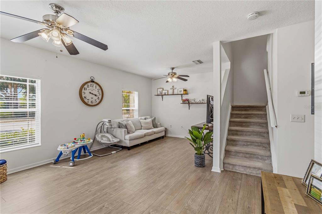 A living room features light wood-look flooring, a gray sofa, and stairs leading upward — 14969 AMBERJACK TERRACE UNIT 14969, BRADENTON, FL