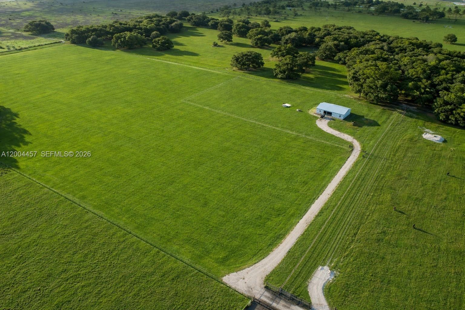 An aerial view shows a large, fenced green pasture with a barn and gravel driveway — 595 Norris Rd, La Belle FL 33935, LA BELLE, FL