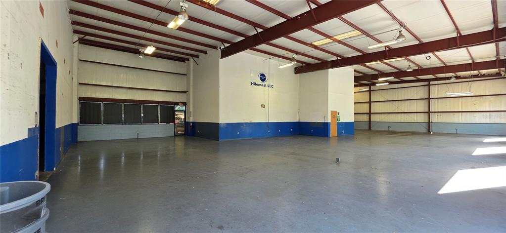 An empty industrial warehouse space features a concrete floor, blue wainscoting, and exposed ceiling beams — 402 CHAIRMAN COURT, DEBARY, FL