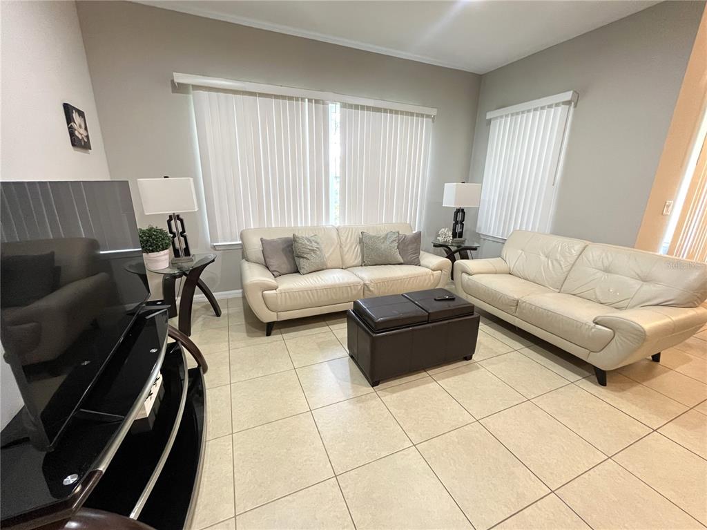 A living room features two cream-colored sofas, a dark ottoman, and tile flooring — 137 NAVIGATION CIRCLE, OSPREY, FL