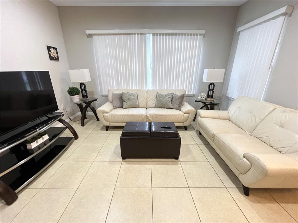 A living room features two cream-colored leather sofas, a dark ottoman, and tile flooring — 137 NAVIGATION CIRCLE, OSPREY, FL