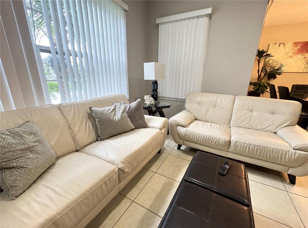A living room features two white leather sofas, a dark ottoman, and vertical window blinds — 137 NAVIGATION CIRCLE, OSPREY, FL