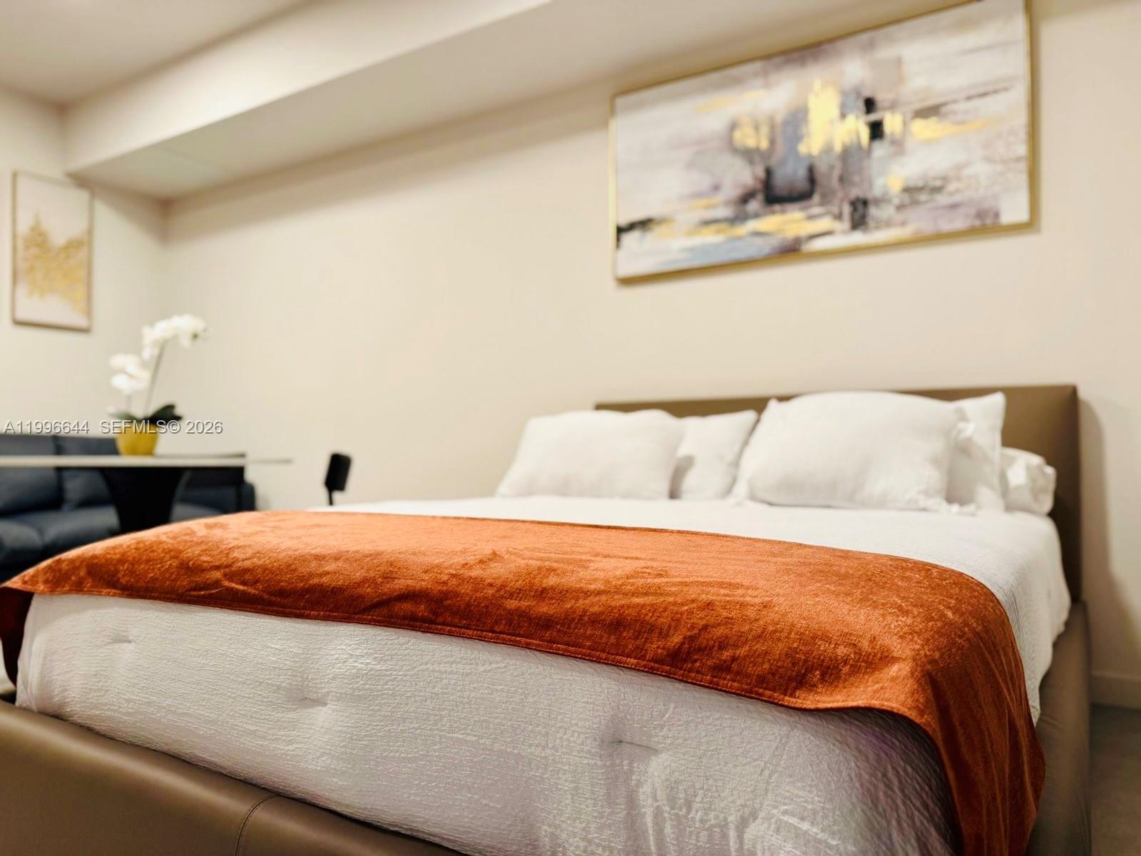 A bedroom features a bed with a rust-colored runner and abstract wall art — 121 NE 5 St # 901B, Miami FL 33132, MIAMI, FL