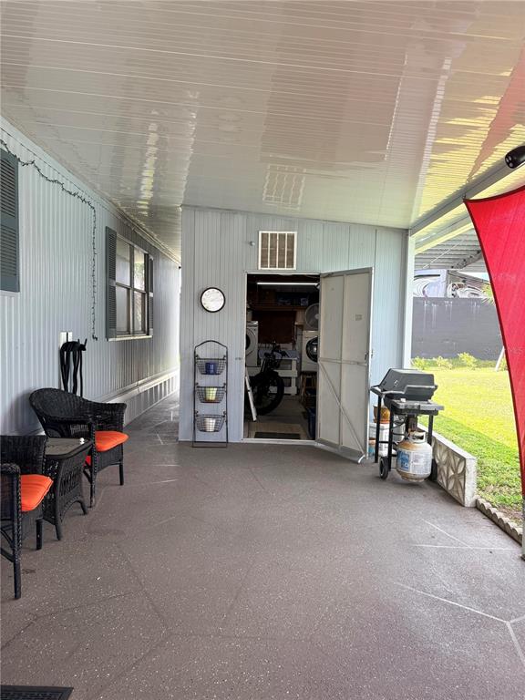 A covered patio features a storage room, outdoor furniture, and a grill on a concrete floor — 2787 BREEZEWOOD DRIVE, NORTH FORT MYERS, FL