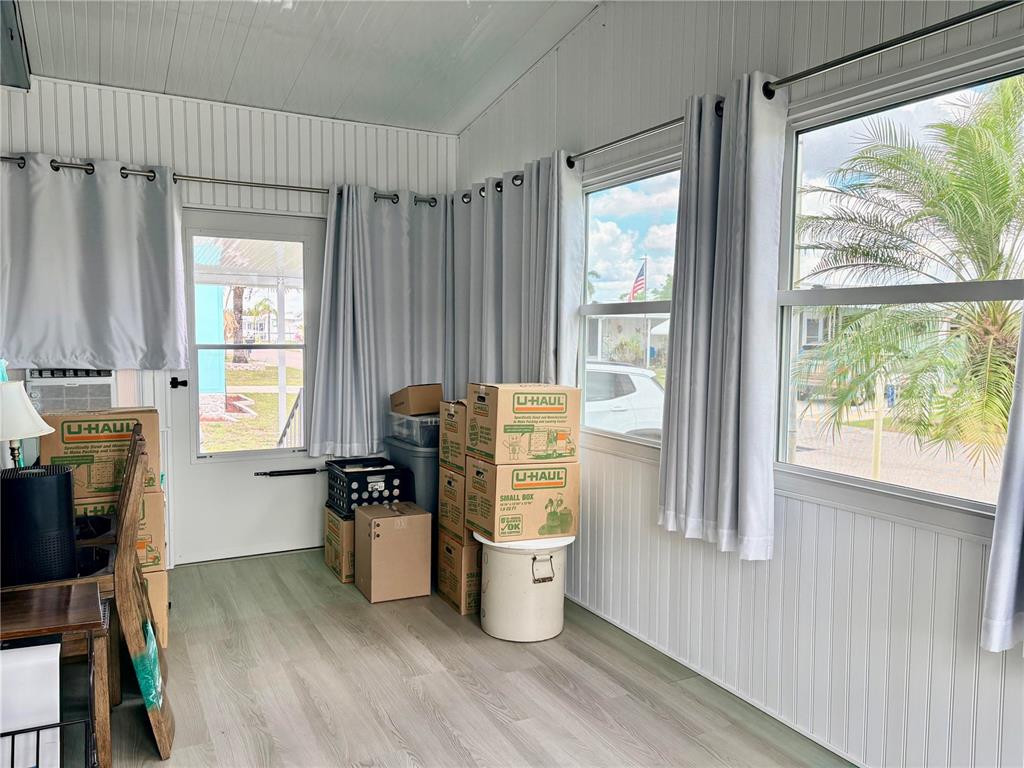 A sunroom with white paneled walls, light wood-look flooring, and several stacked moving boxes — 2787 BREEZEWOOD DRIVE, NORTH FORT MYERS, FL