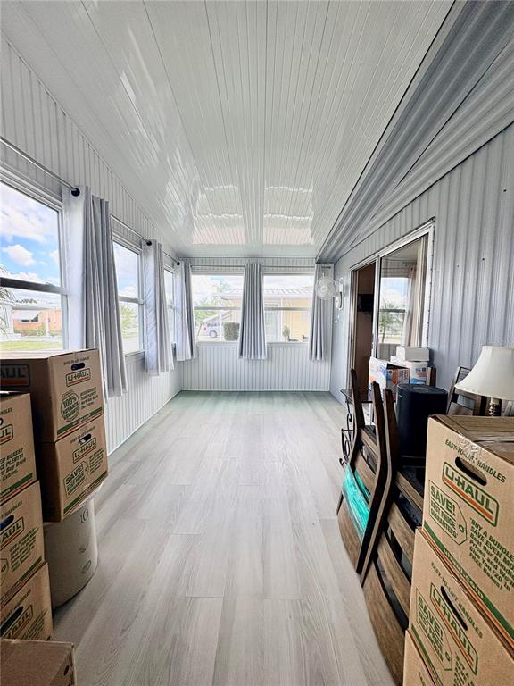 A sunroom features light wood-look flooring, white vertical wall paneling, and large windows with curtains — 2787 BREEZEWOOD DRIVE, NORTH FORT MYERS, FL