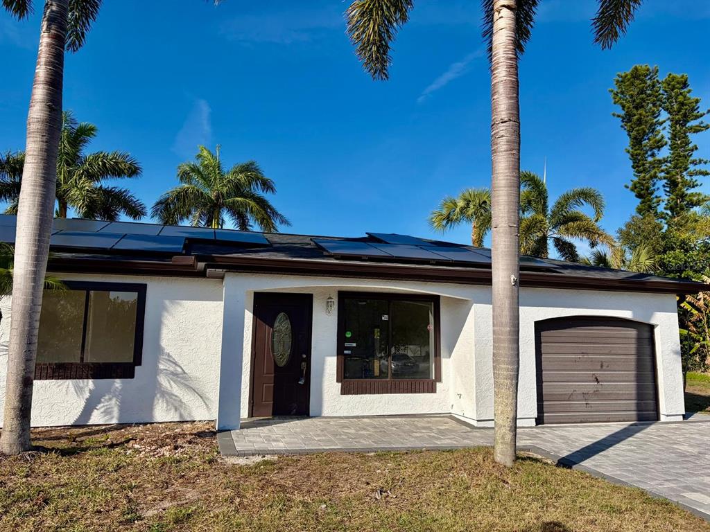 A single-story white house with a dark garage door, solar panels, and palm trees — 6678 ACMAR COURT, NORTH PORT, FL