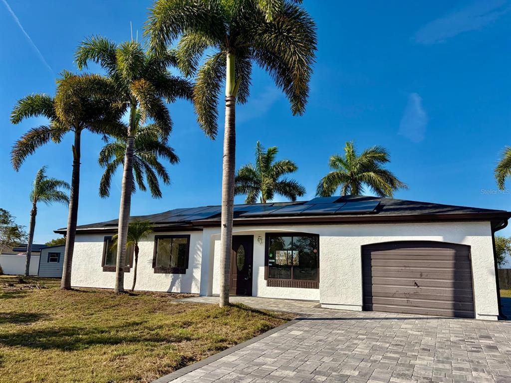 A white single-story house with a paved driveway, solar panels, and several palm trees — 6678 ACMAR COURT, NORTH PORT, FL