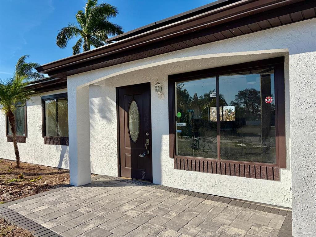 The exterior of a white stucco building features a brown front door and paved patio — 6678 ACMAR COURT, NORTH PORT, FL