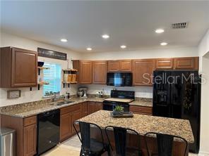 A kitchen features wood cabinets, granite countertops, a kitchen island, and black appliances — 3826 EXETER LANE, LAKELAND, FL
