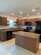A kitchen features wood cabinets, granite countertops, a center island, and black appliances — 3826 EXETER LANE, LAKELAND, FL