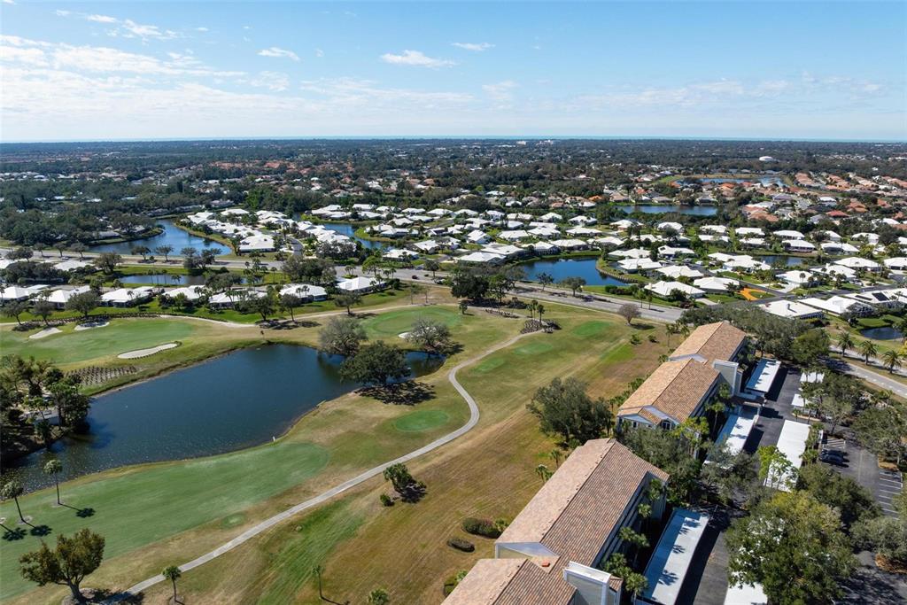 An aerial view shows a golf course, a pond, and residential buildings under a blue sky — 918 WEXFORD BOULEVARD UNIT 918, VENICE, FL
