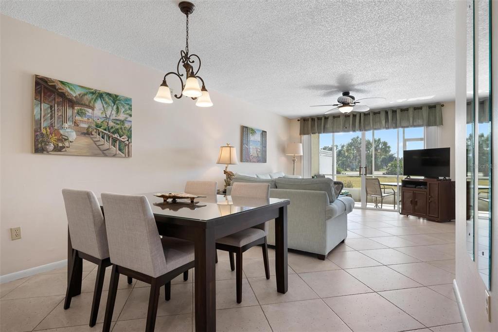A dining area with a glass-top table leads into a living room with tile flooring — 918 WEXFORD BOULEVARD UNIT 918, VENICE, FL